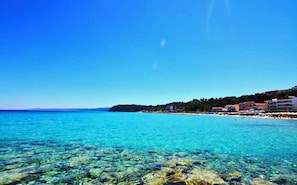 Vista costera con agua turquesa cristalina, costa rocosa y edificios a lo largo de la playa.