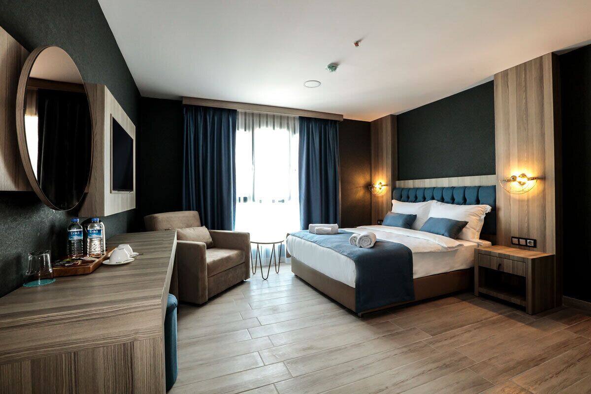 Una habitación de hotel moderna con una cama grande, un escritorio, una silla y una mesita con botellas de agua.