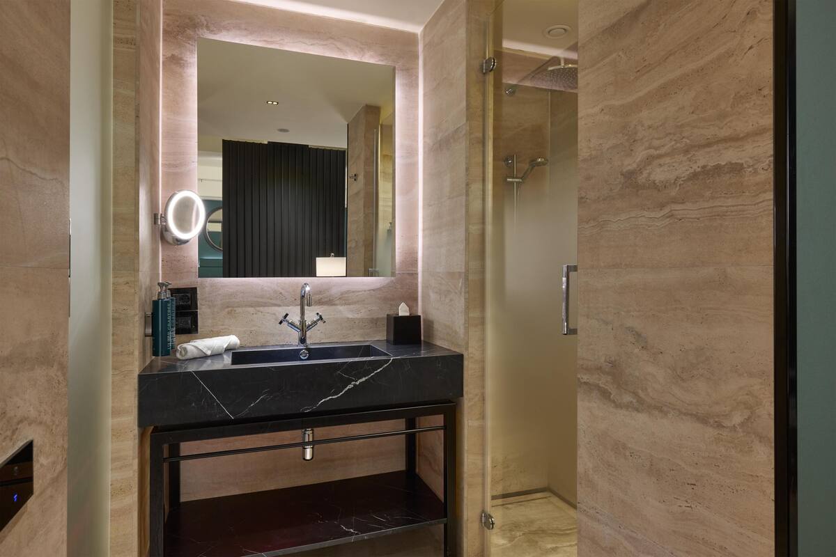 A modern bathroom with a marble sink, a mirror, and a shower area.