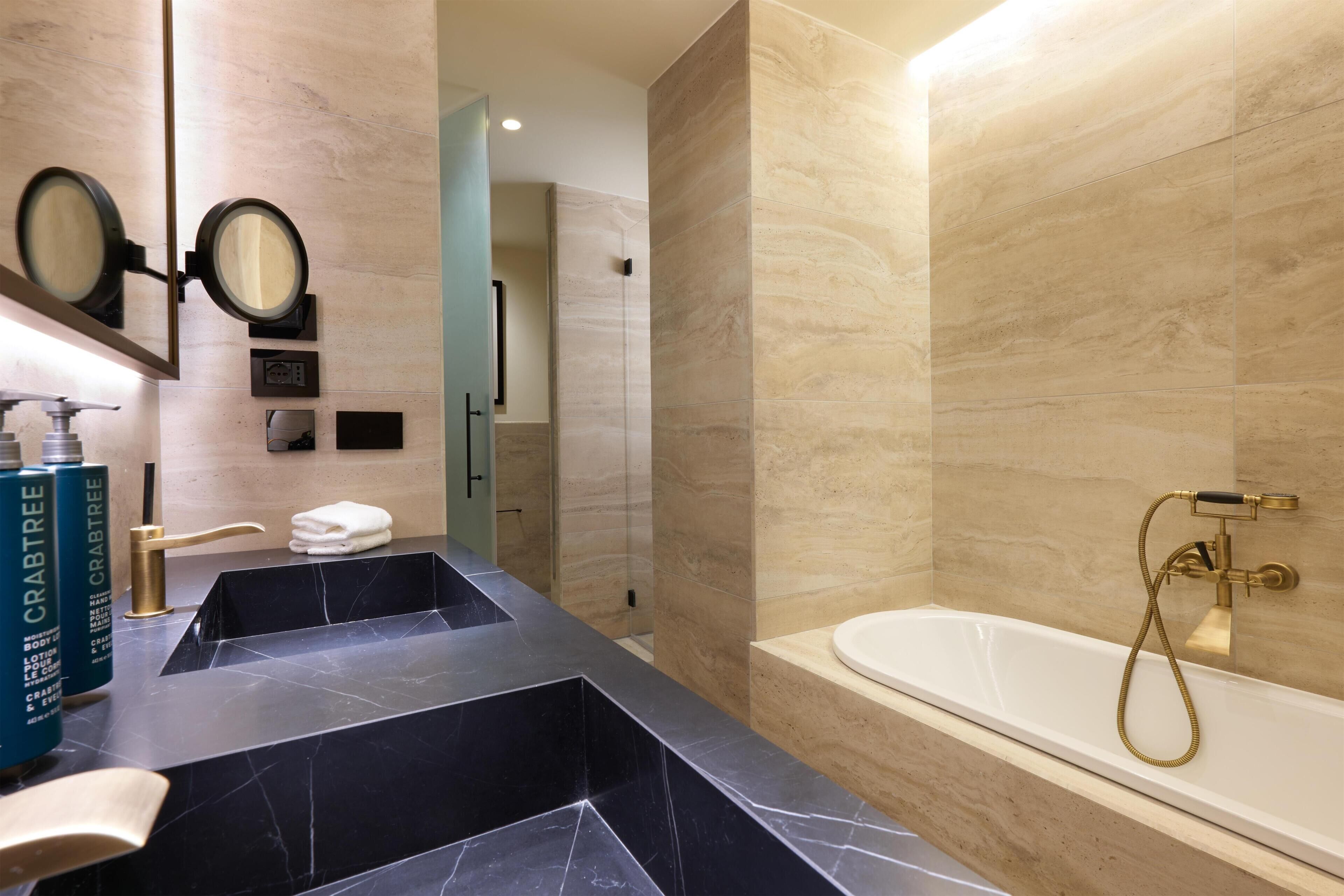 Une salle de bain avec un lavabo en marbre noir, une baignoire blanche et un miroir agrémenté de deux petits miroirs ronds.