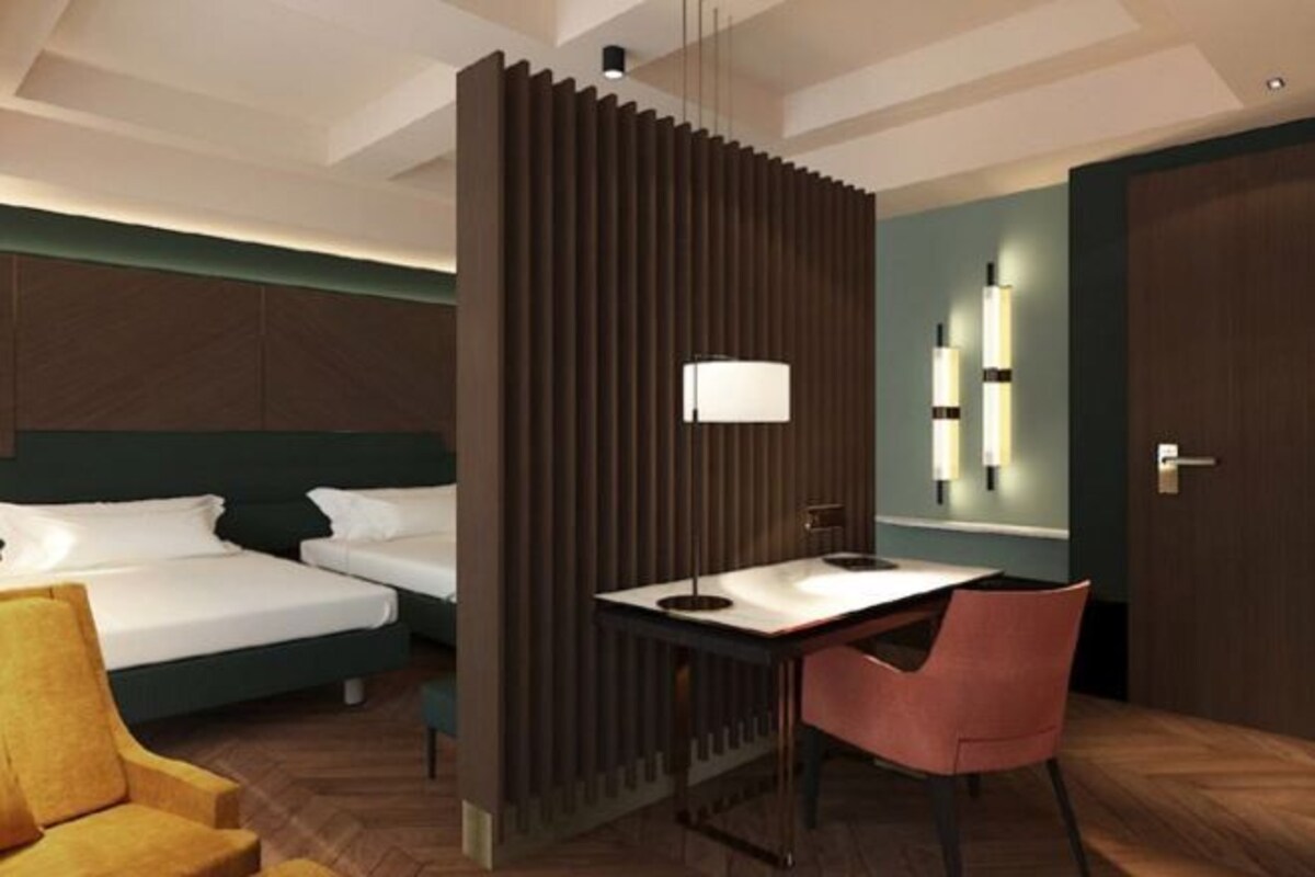 A modern hotel room with a bed, desk, chair, and a partition with vertical slats.