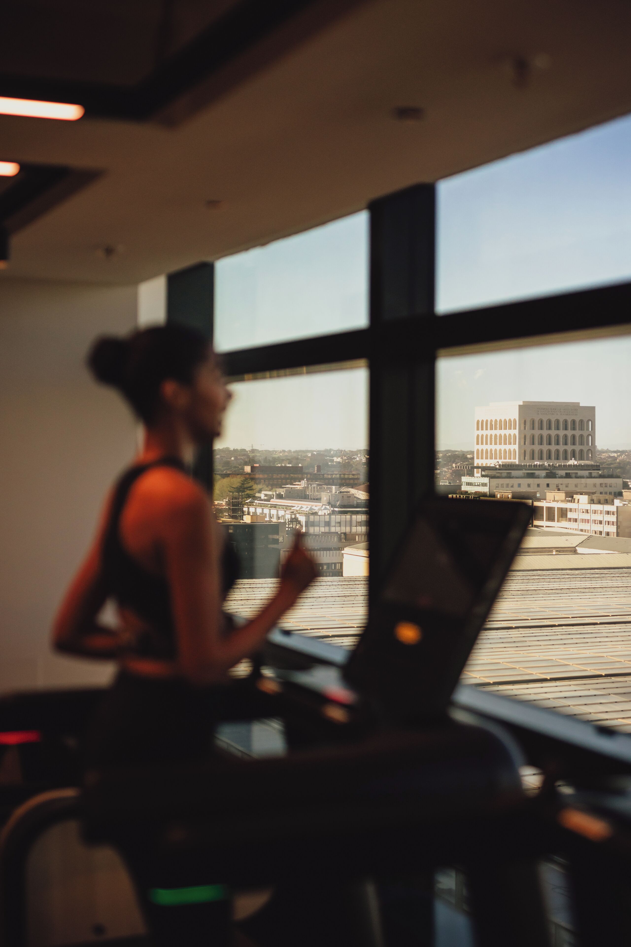 A person running on a treadmill in a room with large windows overlooking a cityscape.