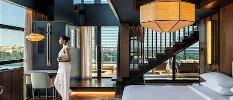 Habitación de hotel moderna con una cama grande, un escritorio, una silla y vistas de la ciudad a través de amplios ventanales.