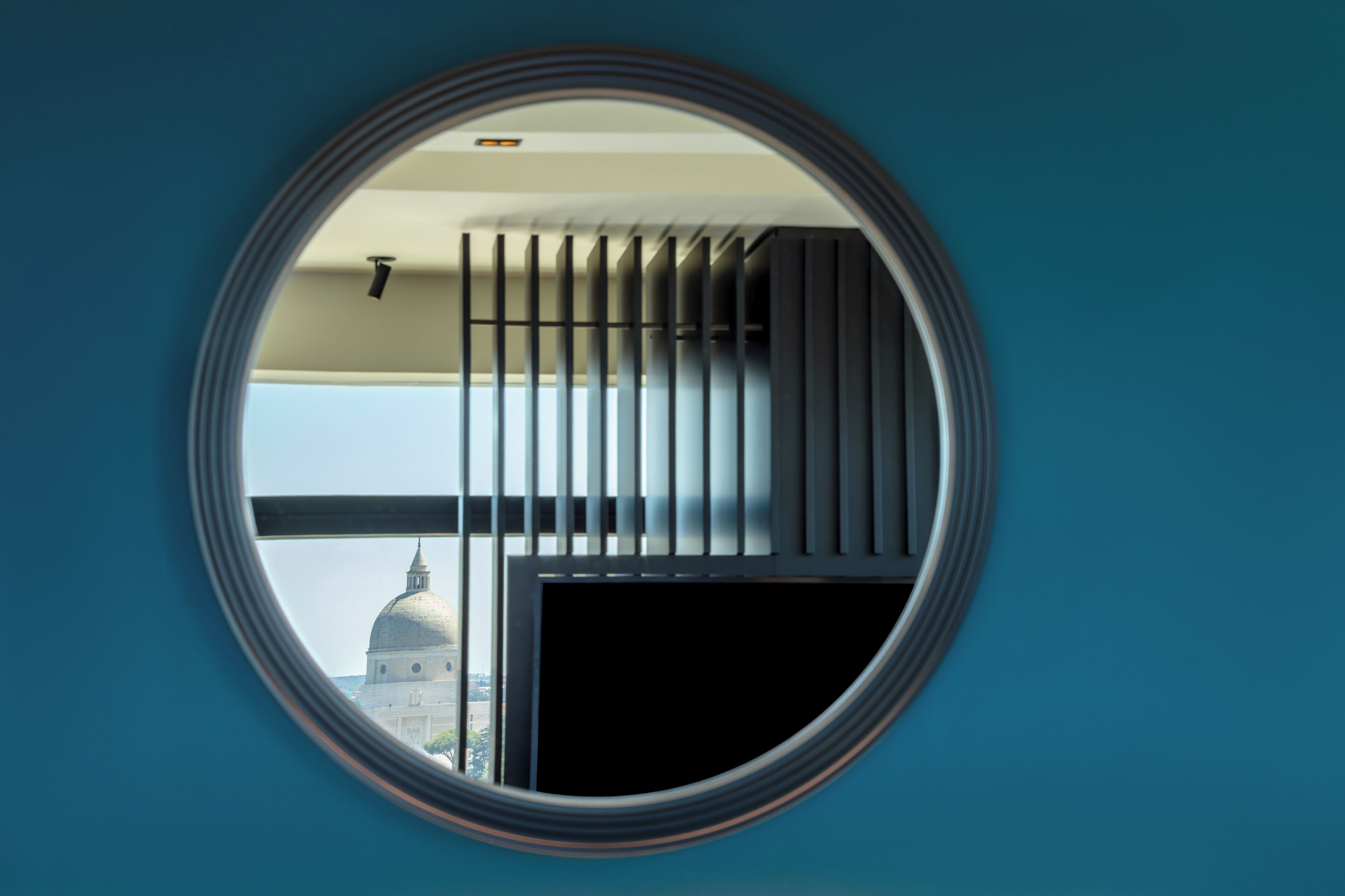 A circular window with a view of a building with a dome and a balcony with vertical bars.