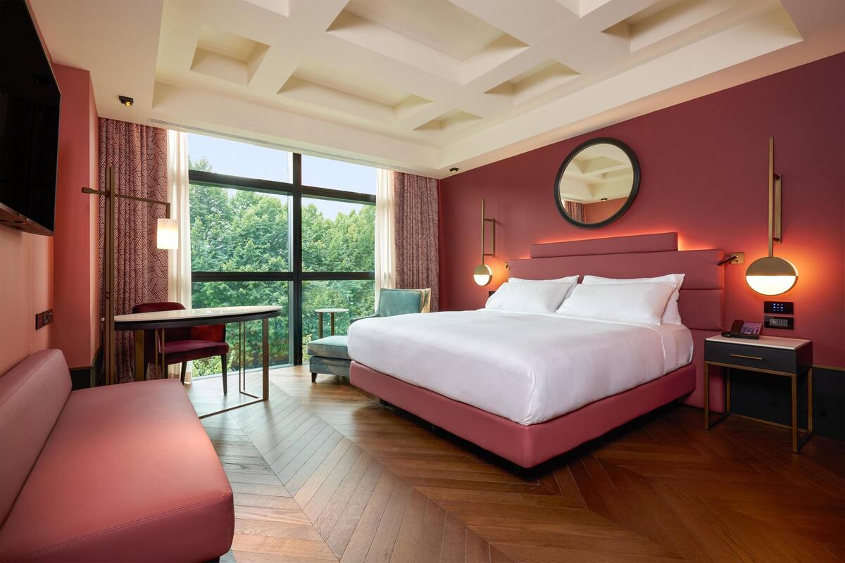 A modern hotel room with a large bed, a desk, and a view of the outdoors.
