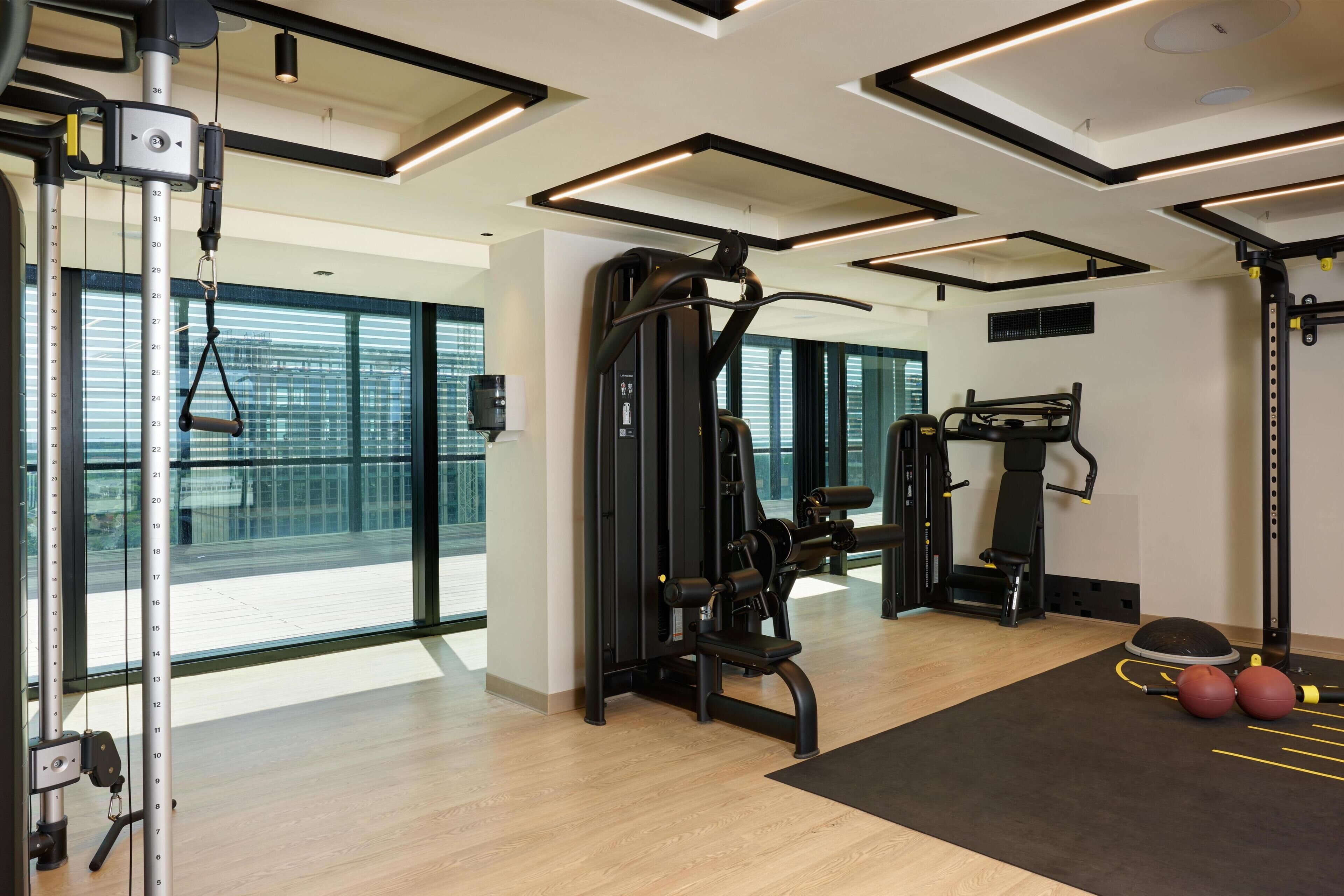 Un gimnasio moderno con equipo de ejercicio, ventanas amplias y suelo de madera.