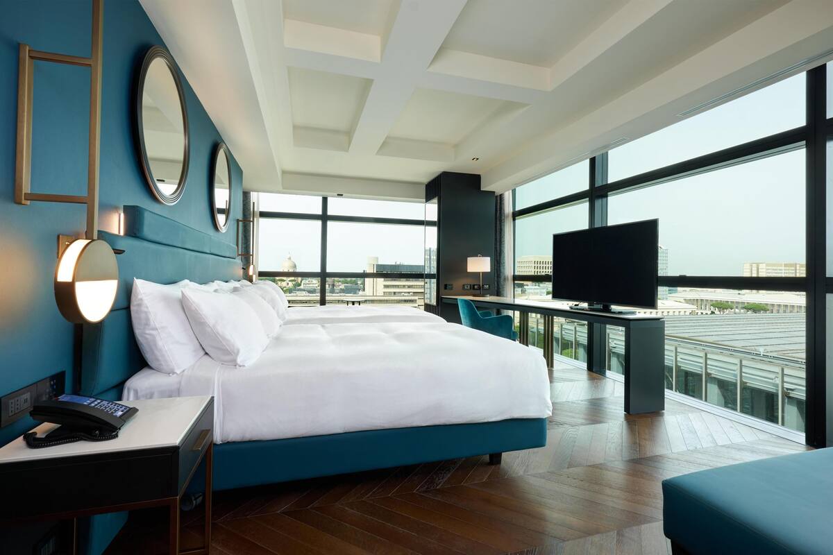 A hotel room with a large bed, a desk with a TV, a phone, and a view of the city.