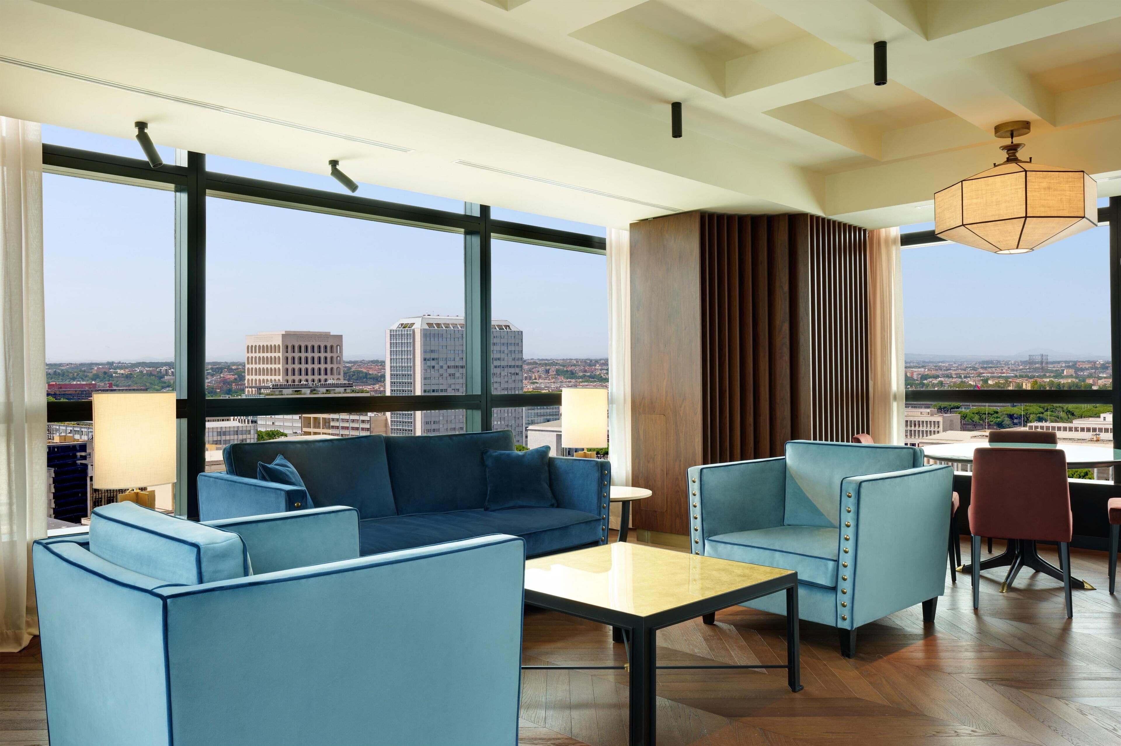 Una habitación de hotel moderna con un ventanal grande, un sofá, una mesa y una silla.