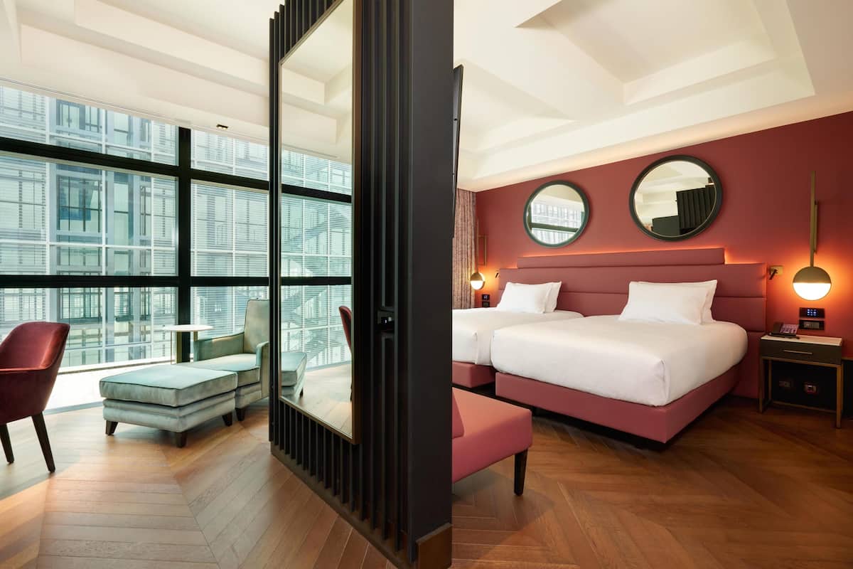 A hotel room with a large window, a bed, a chair, and a small table.