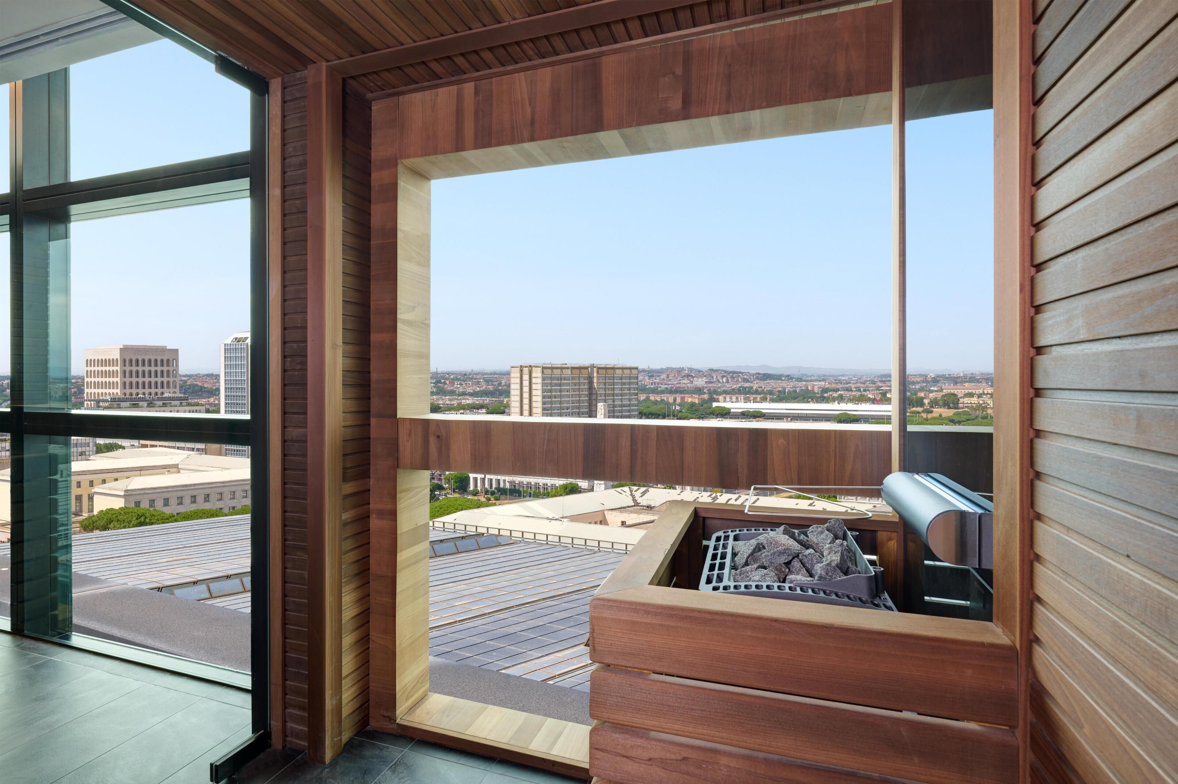 Un interior moderno con amplios ventanales, un banco de madera y vista a la ciudad.