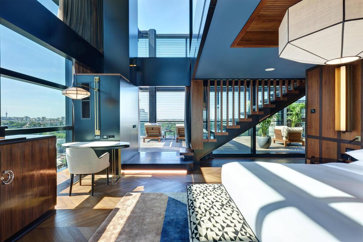 A modern hotel room with a large bed, a dining area, and a view of the city.