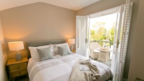 Ein Schlafzimmer mit einem Bett, Nachttischlampen, einem Fenster mit Jalousien und Blick ins Freie.