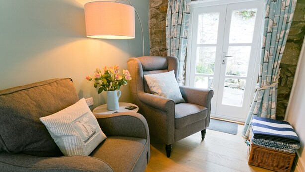 Un salon chaleureux avec un canapé gris, un fauteuil assorti, une table d’appoint sur laquelle est posé un vase de fleurs et un panier en osier.