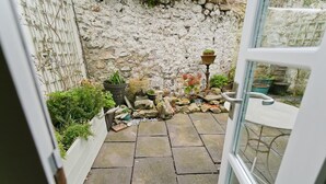 Une terrasse dallée de pierres, agrémentée de plantes en pot et d’une petite table, qui mène à un mur de pierres.