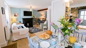 Un salon chaleureux avec une cheminée, un coin repas avec une table mise pour le petit-déjeuner, et une cuisine visible au fond.
