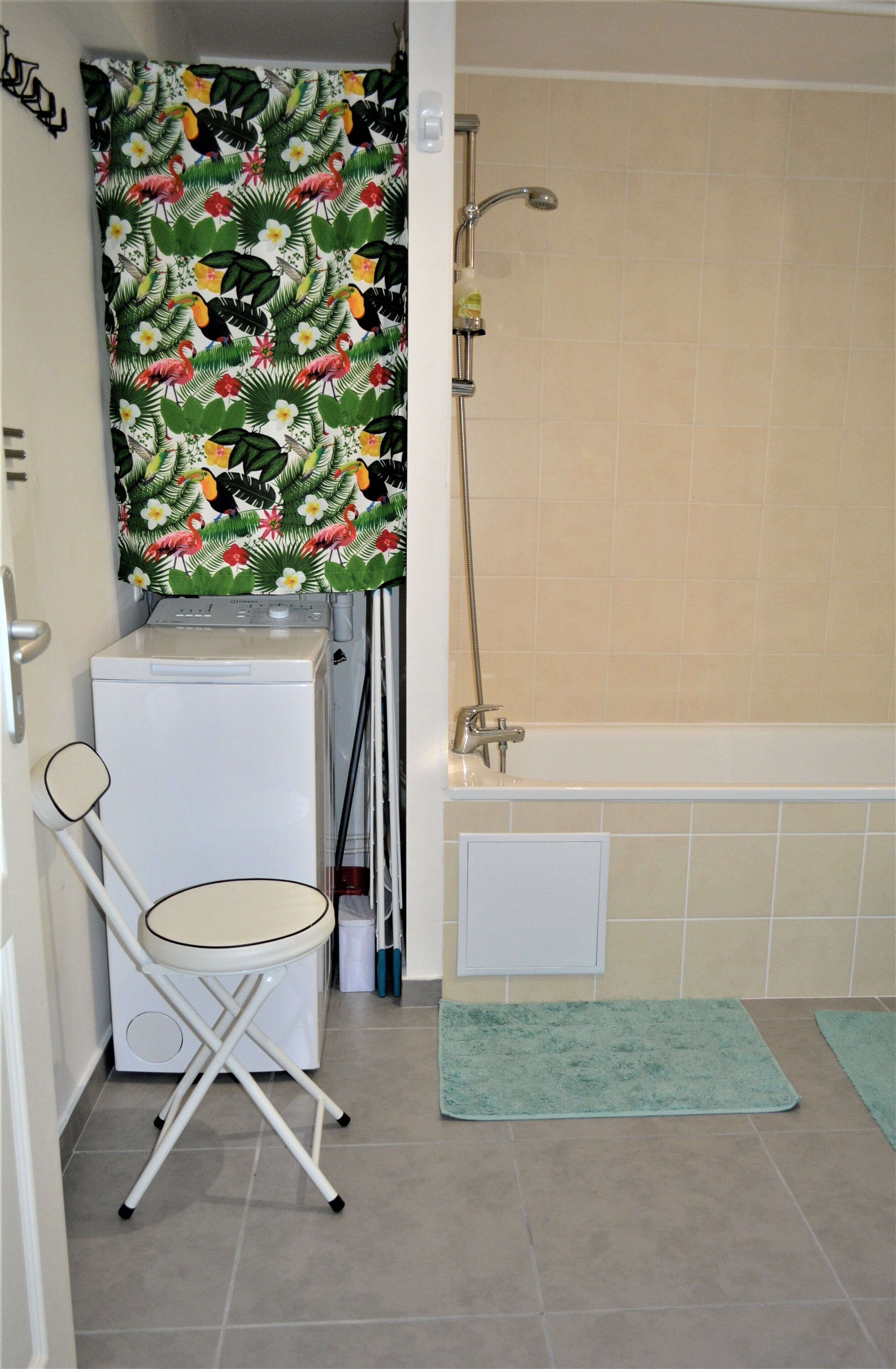 A bathroom with a shower, a washing machine, and a folding chair.