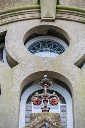 A stone building with a circular window and a decorative metal fixture. - Cribinau (Ty Croes)