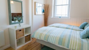 A bedroom with two beds, a window, a mirror, and a shelf with baskets. - Cribinau (Ty Croes)