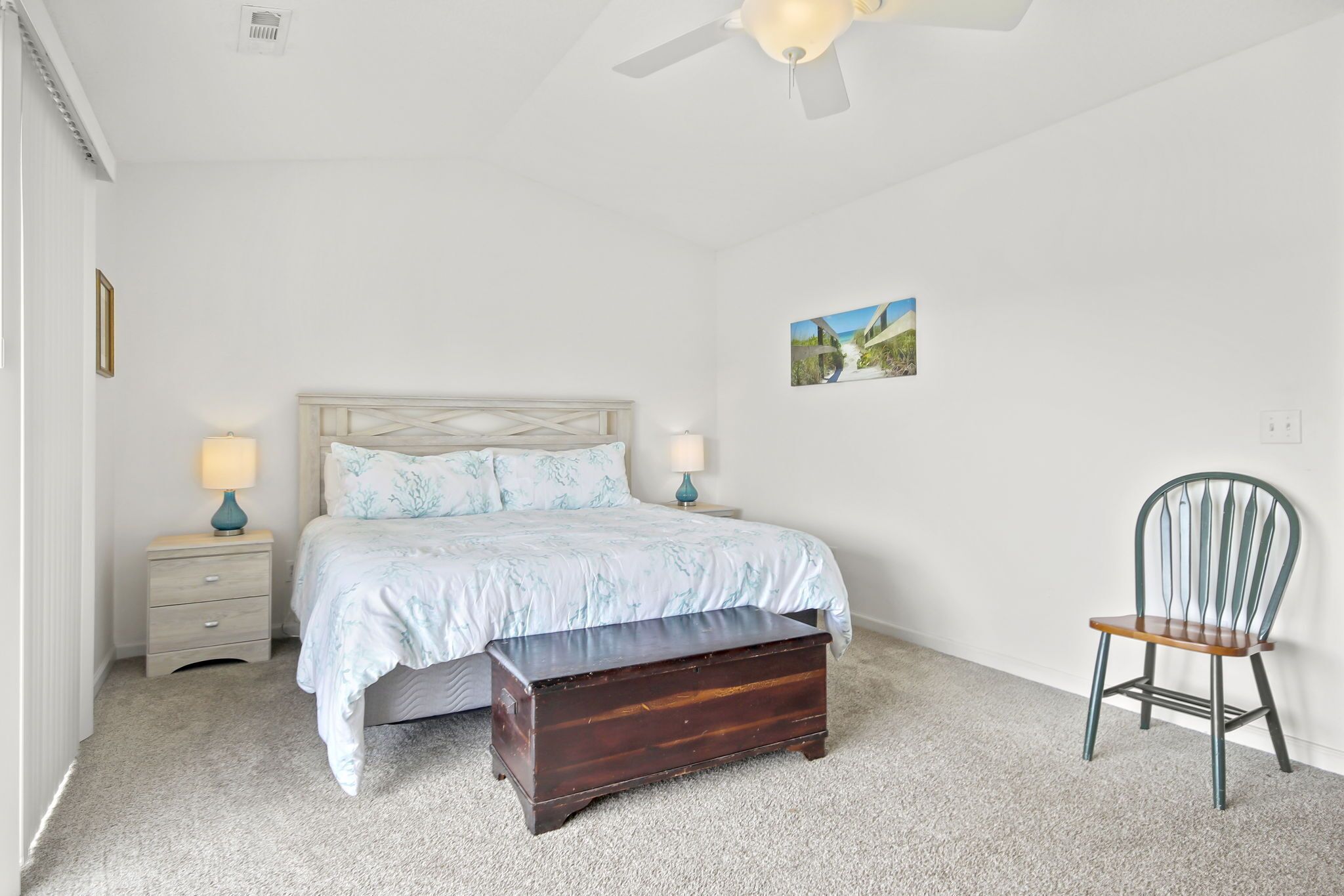 A bedroom with a bed, bedside tables, a bench, a chair, and a ceiling fan.