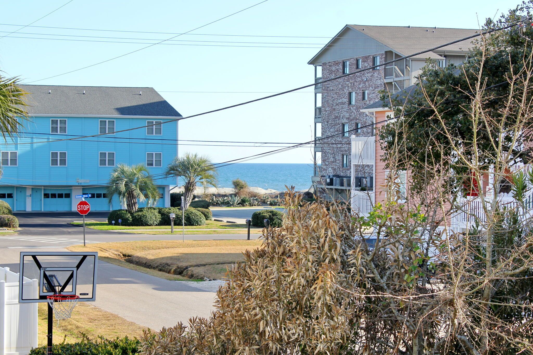A residential area with a blue building, a stop sign, a basketball hoop, and a view of the sea.