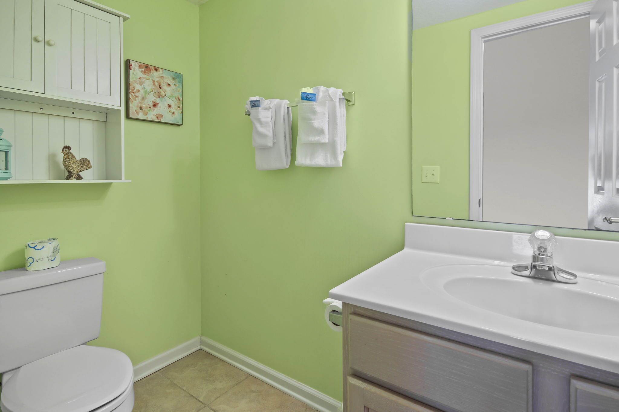 A bathroom with a toilet, sink, and a cabinet with a decorative item.