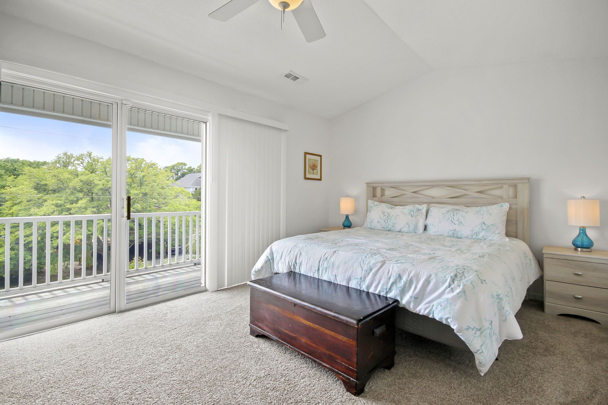 A bedroom with a bed, a nightstand, a bench, a ceiling fan, and a sliding glass door to a balcony.