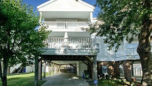 A two-story building with a balcony on the upper floor, a covered entrance, and a brick foundation. - Sea Chique | Ocean View Beach House with Private Pool and Hot Tub (Surfside Beach)