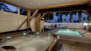 A hot tub in an outdoor patio area with a pool, wooden deck, and a white fence. - Sea Chique | Ocean View Beach House with Private Pool and Hot Tub (Surfside Beach)
