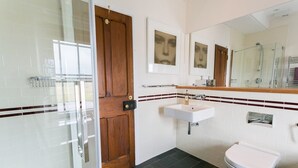 Un baño con puerta de madera, lavamanos blanco y cabina de ducha con mampara de vidrio.