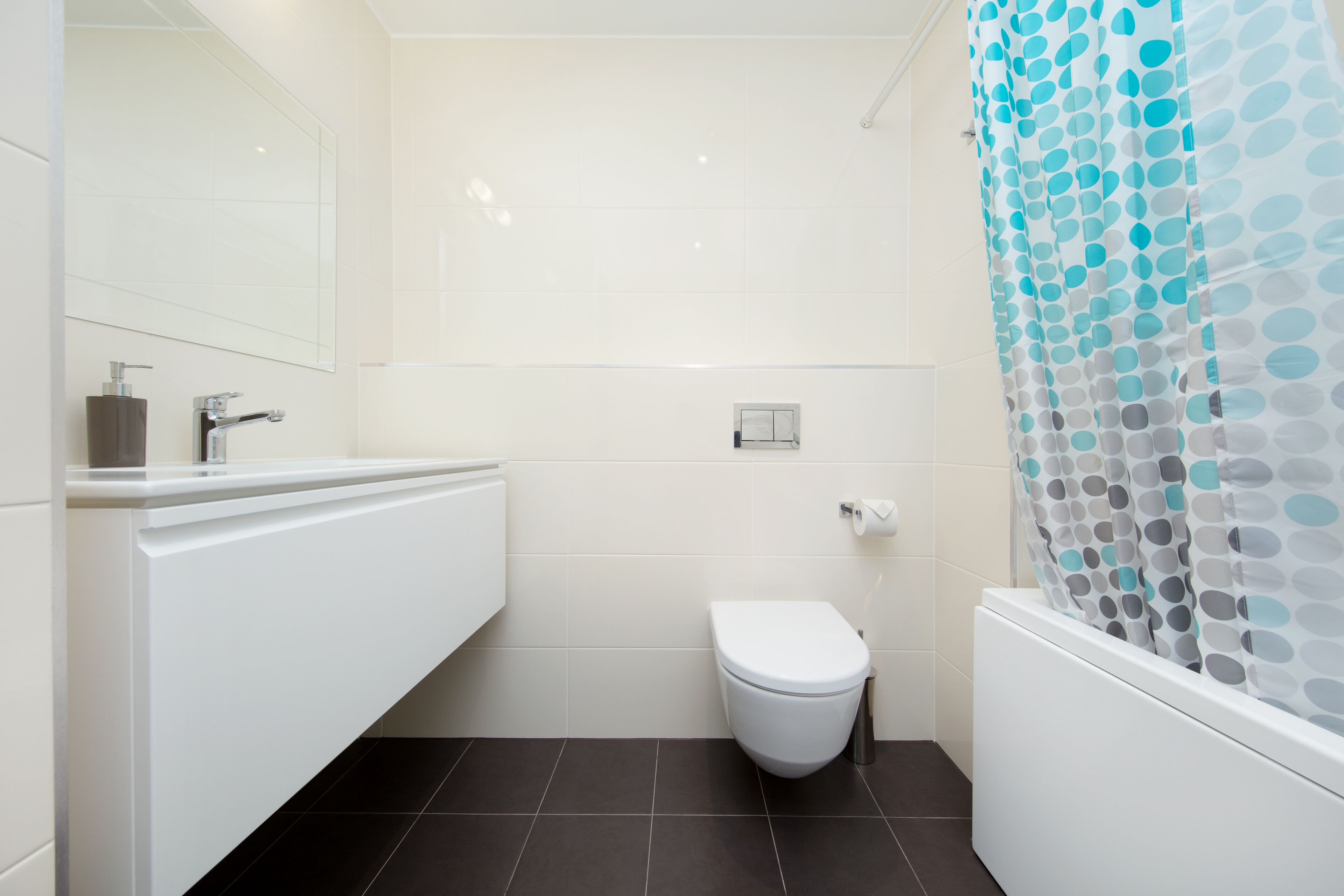 A modern bathroom with a white toilet, a white sink, and a shower curtain with a polka dot pattern.