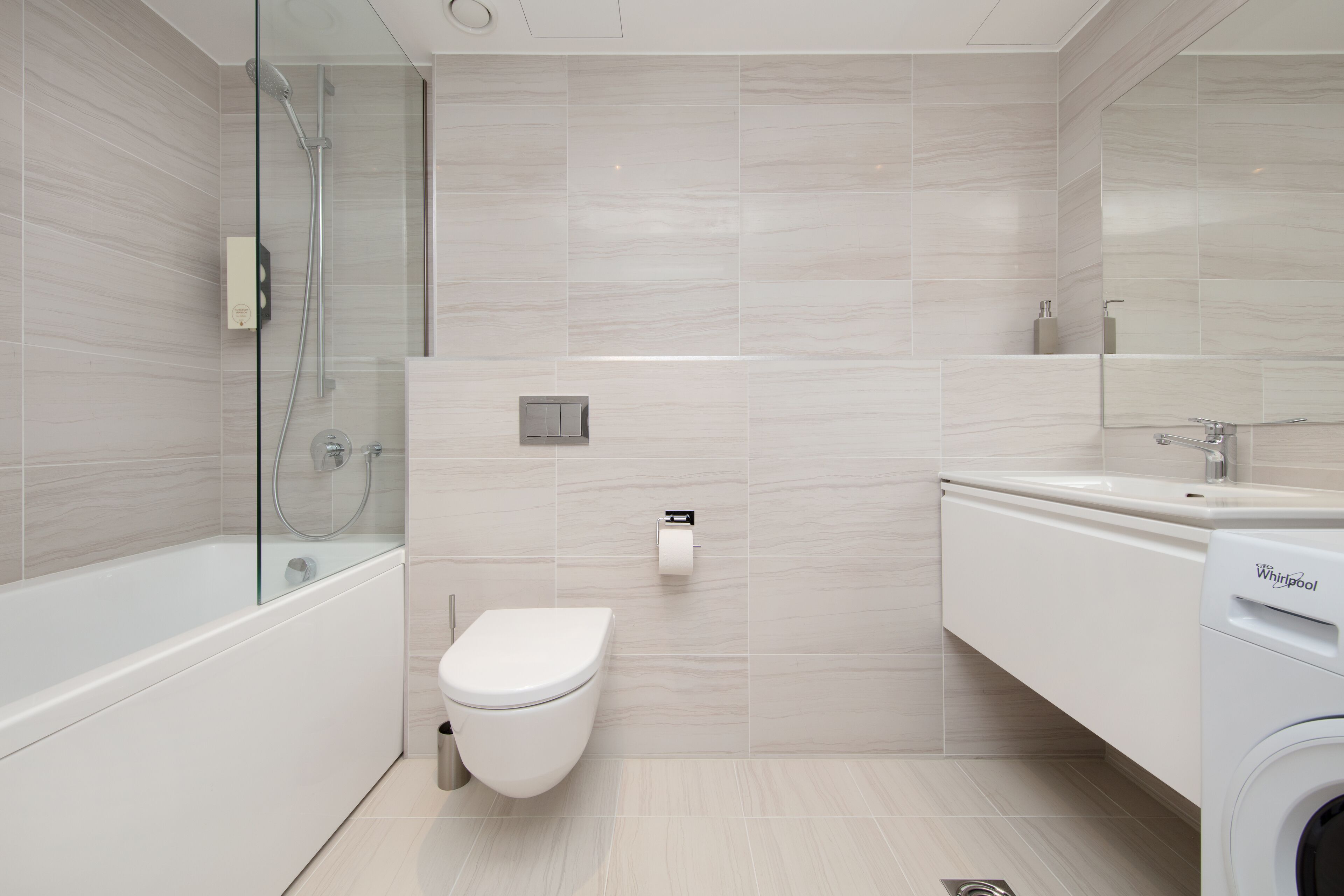 Un bany modern amb dutxa de vidre, vàter, rentapous i una rentadora Whirlpool.