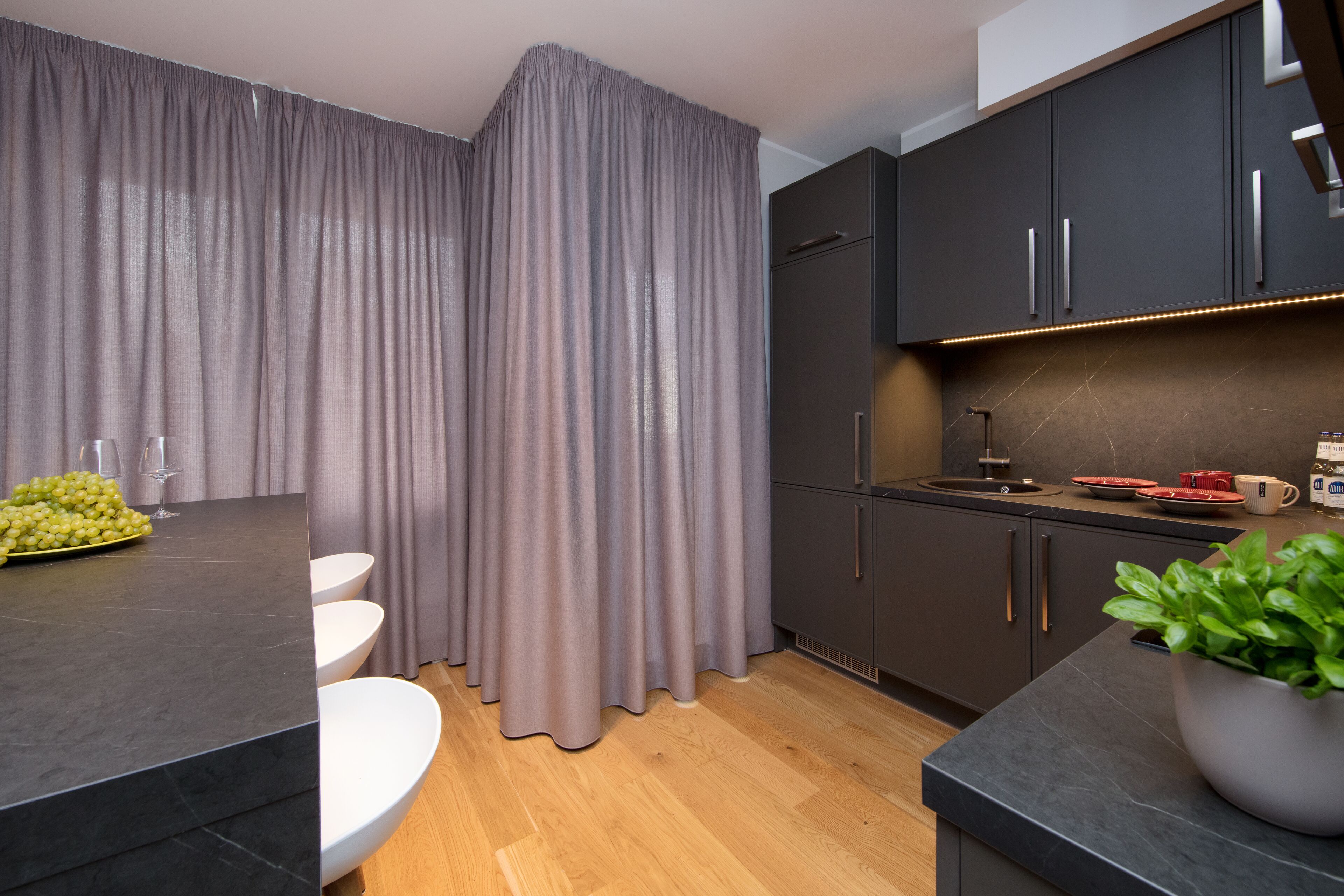 A modern kitchen with dark cabinets, a marble countertop, and a wooden floor.