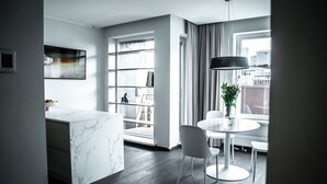 Une cuisine moderne dotée d’un plan de travail en marbre, d’un coin repas avec une table ronde et des chaises, et offrant une vue sur la ville grâce à de grandes fenêtres.