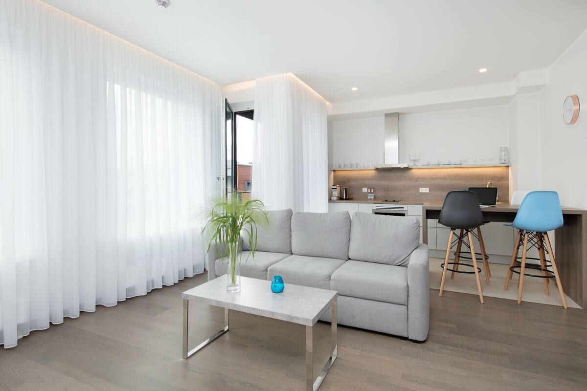 Ein modernes Wohnzimmer mit einer Couch, einem Couchtisch und einer Küche im Hintergrund.
