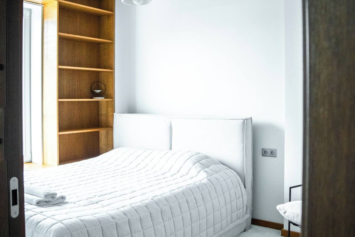 Ein Schlafzimmer mit einem großen Bett, einer Holzregaleinheit, einer weißen Pendelleuchte und einem kleinen Nachttisch.
