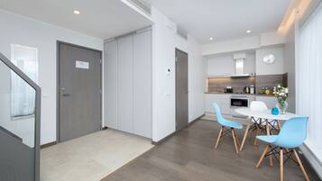 Une cuisine moderne avec des meubles blancs, un coin repas avec des chaises bleues et un escalier menant à un autre niveau.