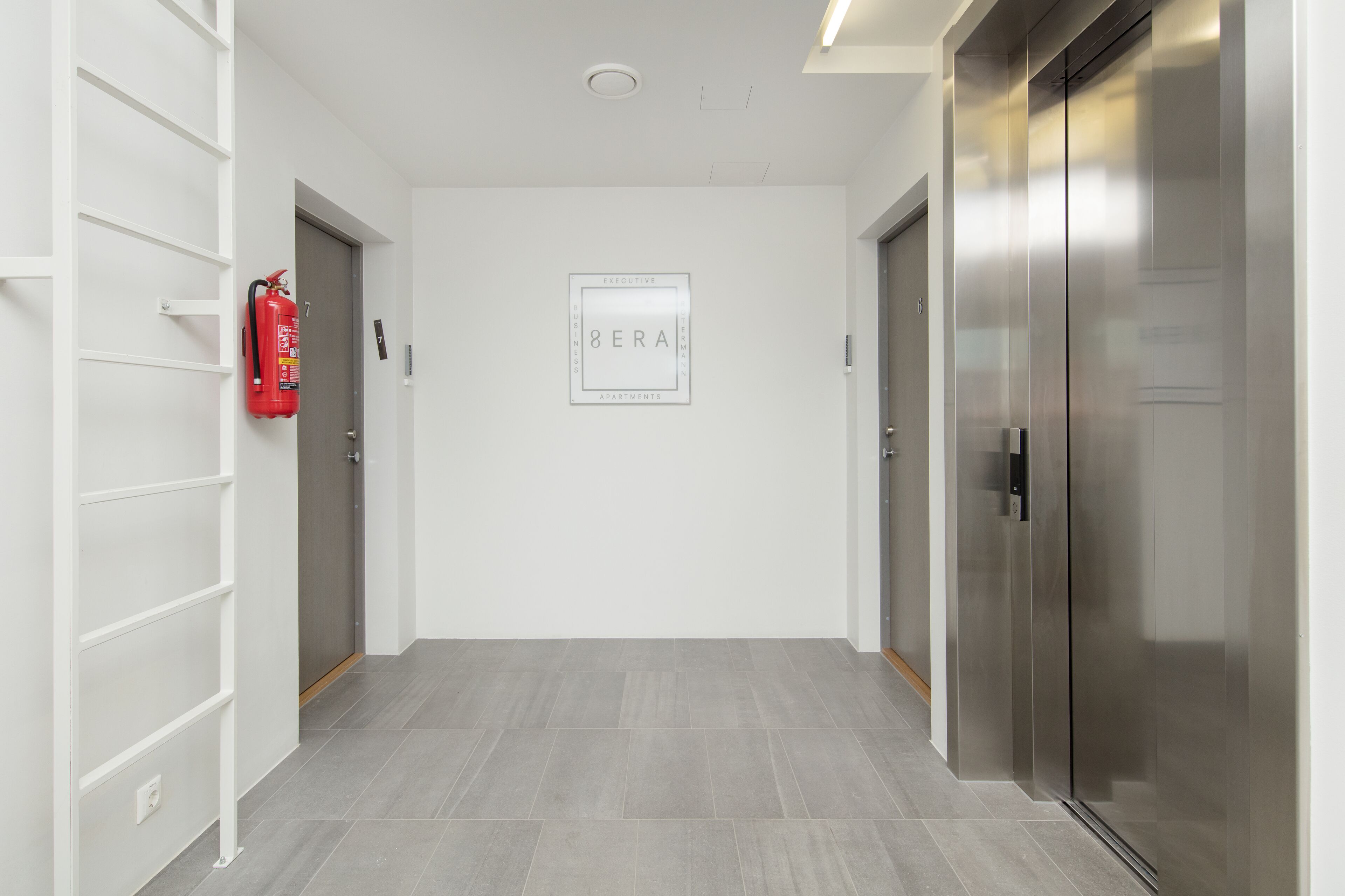 A hallway with a fire extinguisher, a framed sign, and a modern elevator.