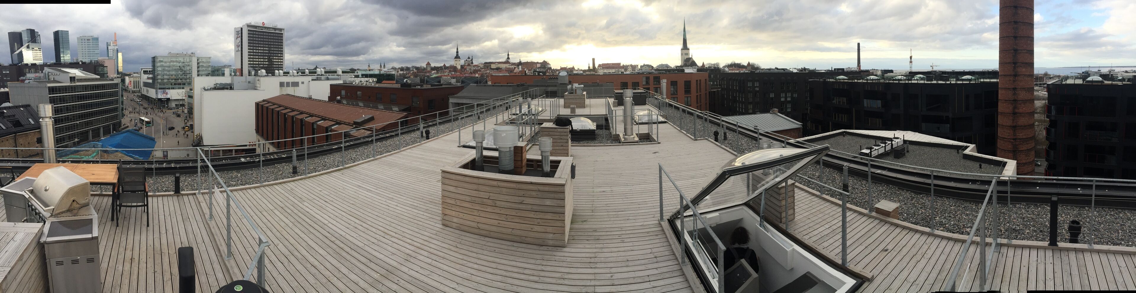 A rooftop terrace with a grill, seating area, and a view of the cityscape.