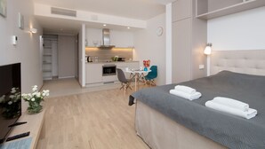 Une chambre d’hôtel moderne dotée d’un grand lit, d’un bureau avec un ordinateur, d’un petit coin cuisine et d’une table à manger.