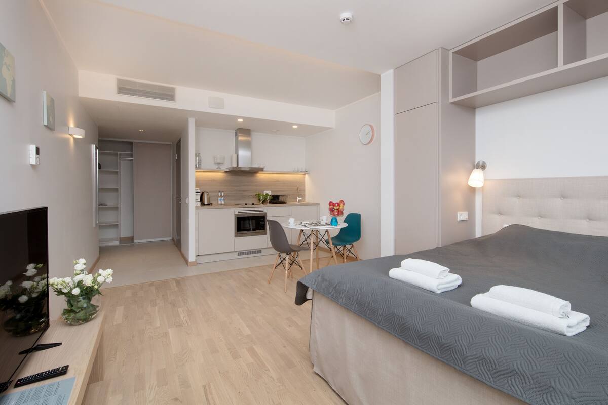 Ein modernes Hotelzimmer mit einem großen Bett, einem Schreibtisch mit Computer, einer kleinen Küchenzeile und einem Esstisch.