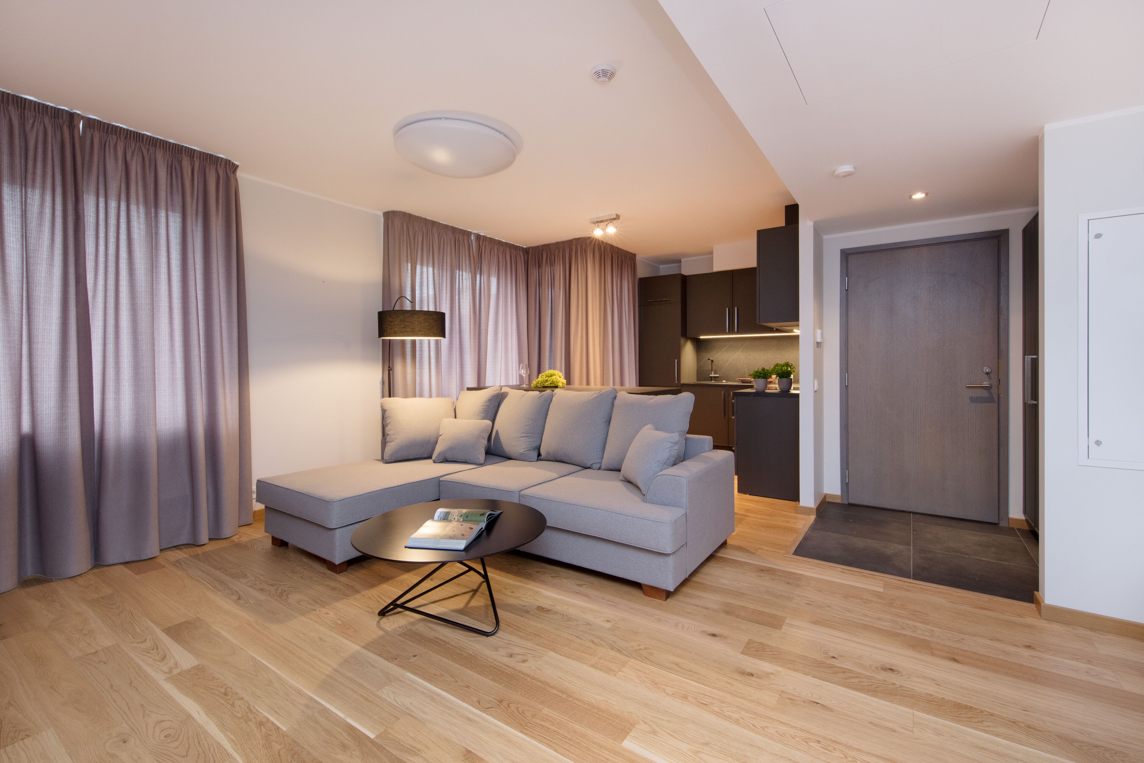 A modern living room with a sectional sofa, a coffee table, and a dining area with a kitchen in the background.