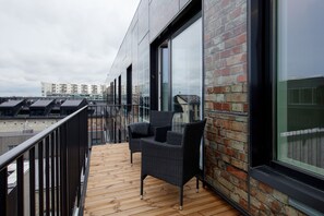 A balcony with wicker furniture, a wooden floor, and a brick wall with large windows. - 8ERA Business Executive Rotermanni Apts (Tallinn)