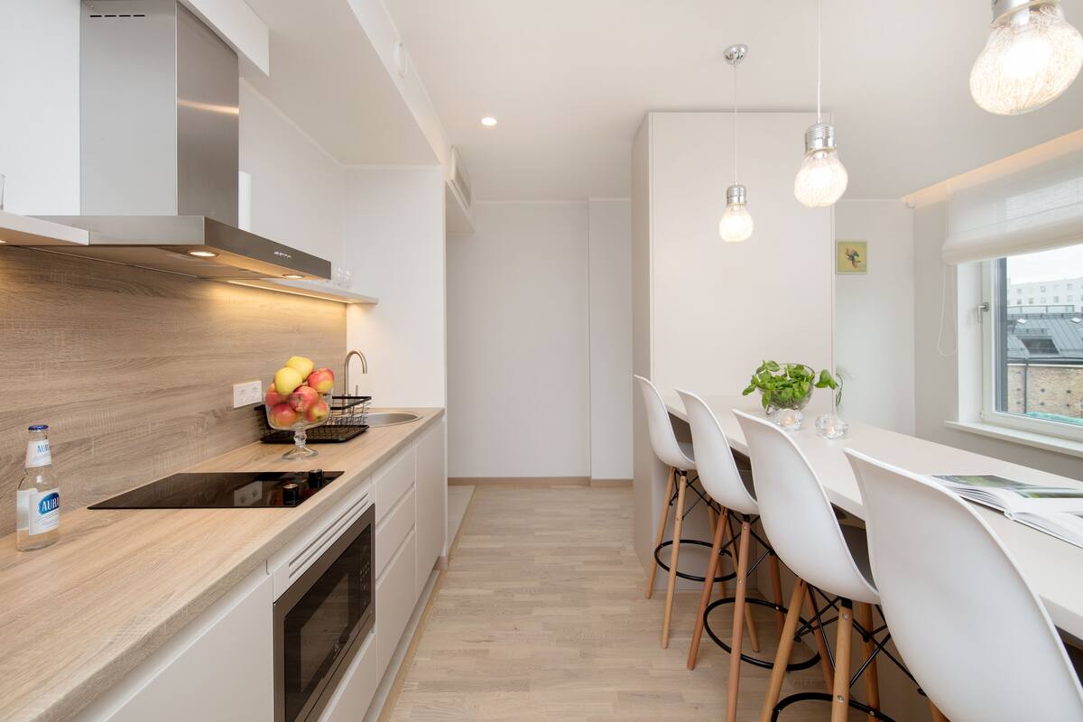Eine moderne Küche mit Holztischplatte, Edelstahlgeräten und einem Essbereich mit weißen Stühlen und einem Tisch.