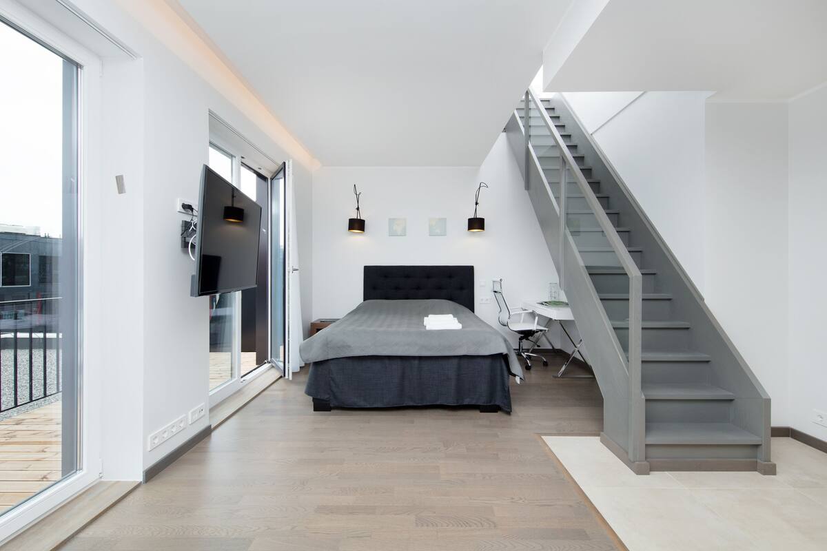 Ein modernes Schlafzimmer mit einem großen Bett, einer Treppe und einem an der Wand befestigten Fernseher.