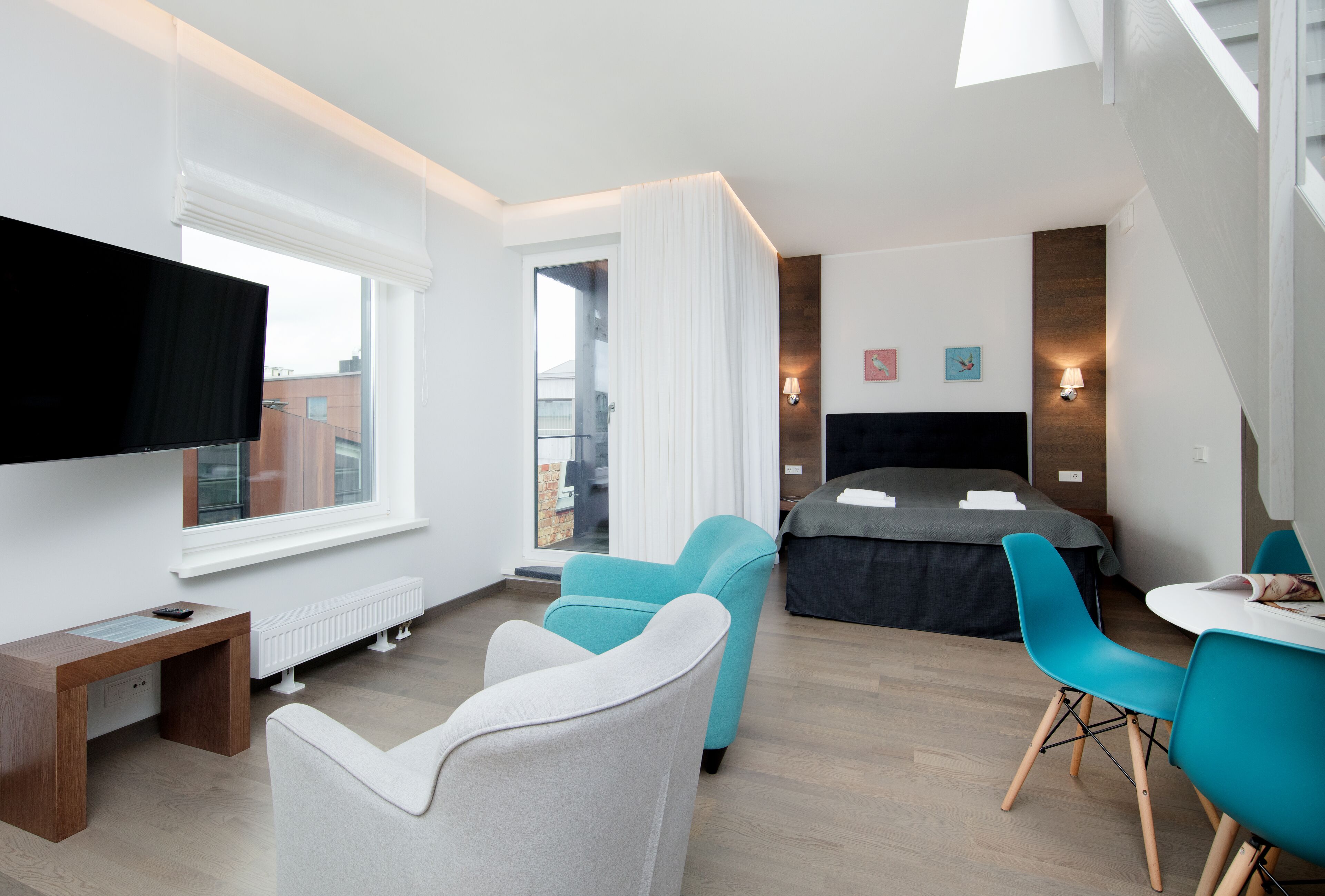 A modern hotel room with a large bed, a desk with a computer, a TV, and two chairs.