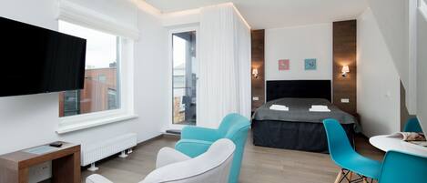 A modern hotel room with a large bed, a desk with a computer, a TV, and two chairs.