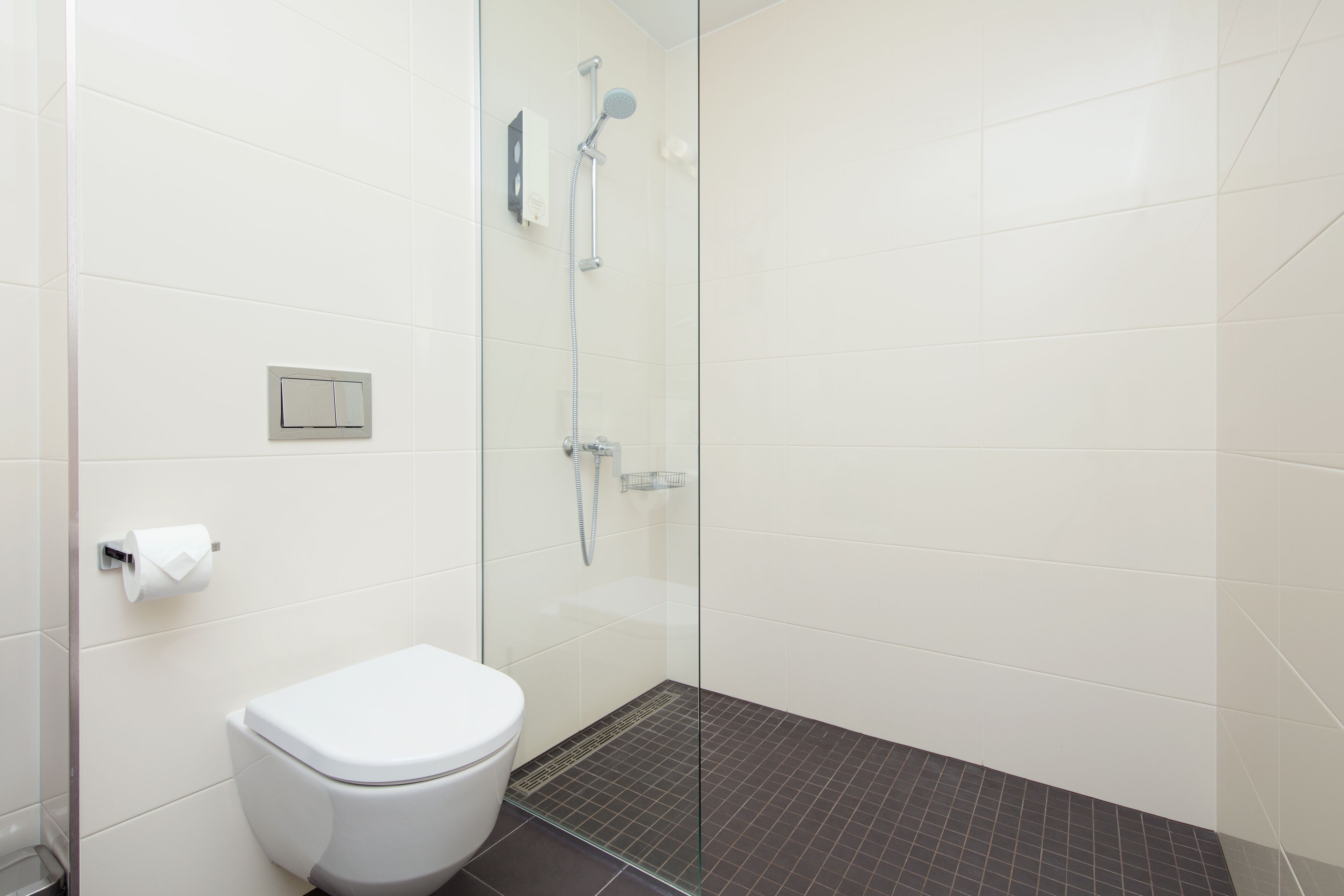 Une salle de bain avec des toilettes, une douche à parois de verre et un carrelage au sol.