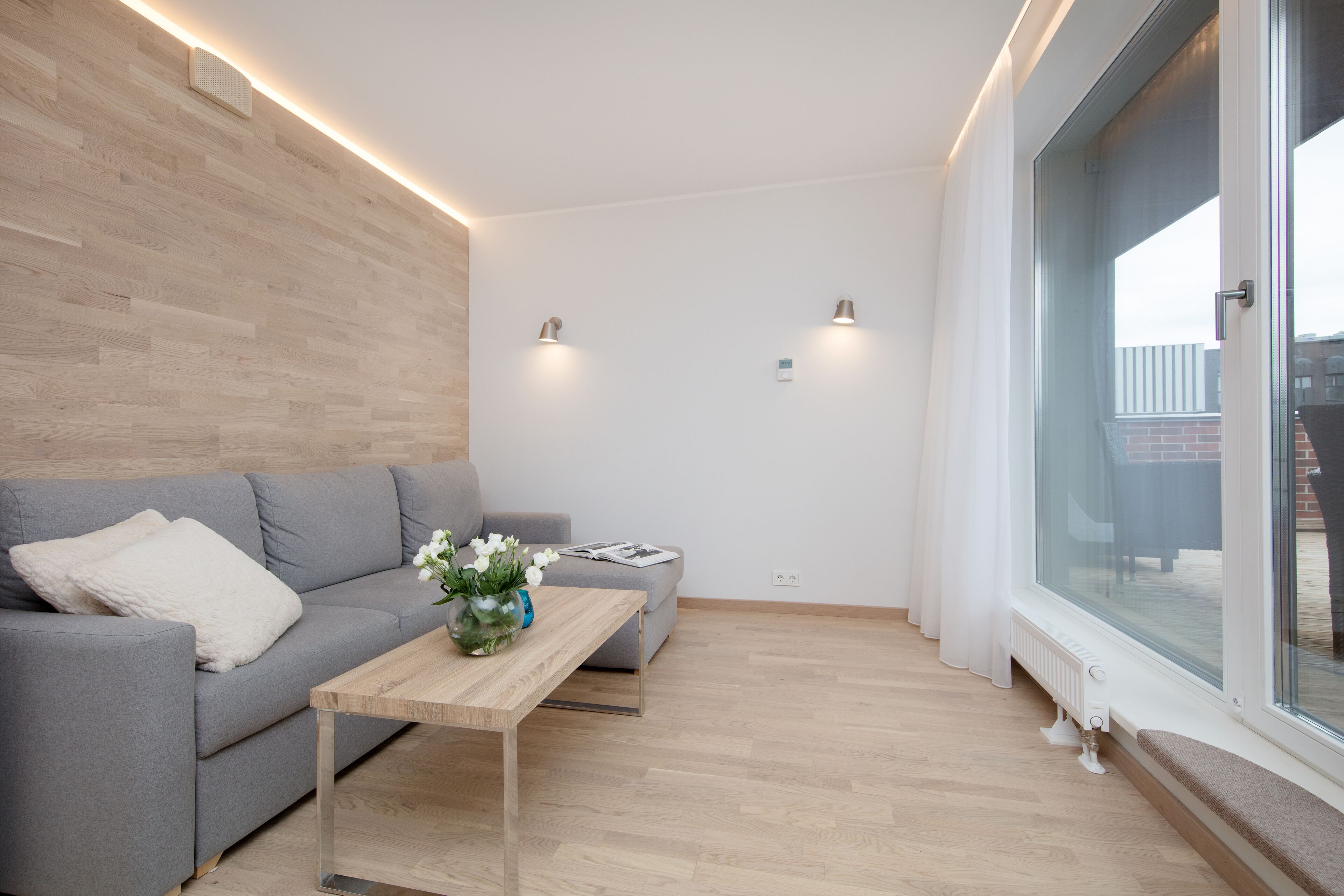 Un salon moderne avec un canapé gris, une table basse en bois et une grande fenêtre.