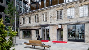 Un bâtiment en pierre avec un banc devant, une devanture de magasin portant l’inscription « PERFECTSHOES », et un tapis rouge menant à l’entrée.