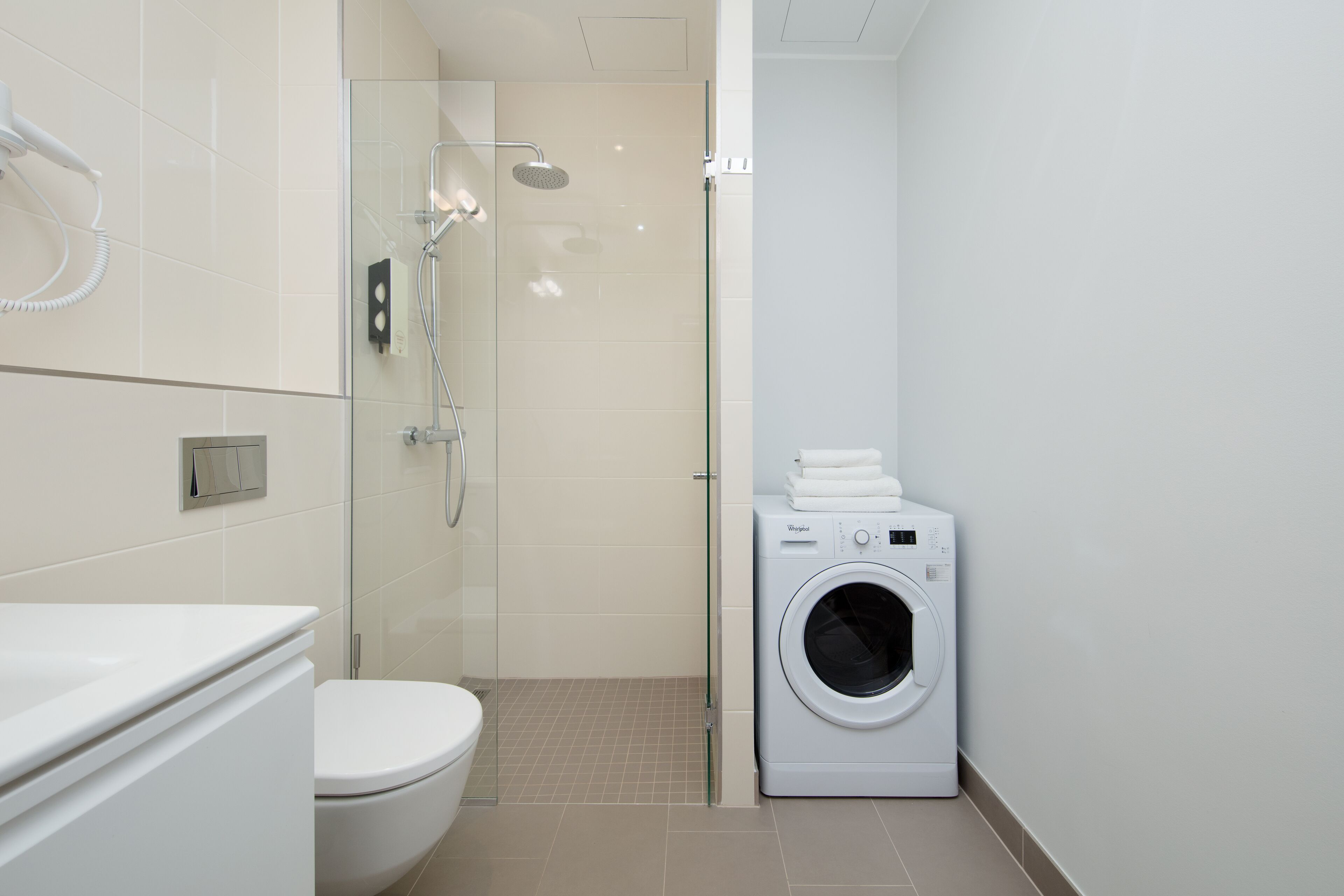 Un bagno moderno con cabina doccia in vetro, un water e una lavatrice a carica frontale.